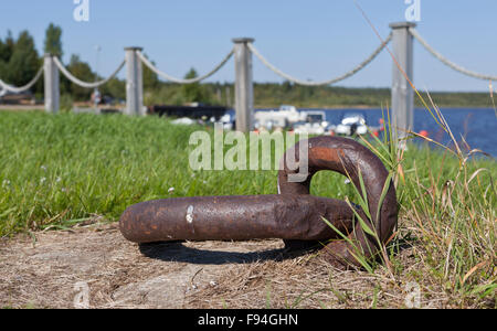 Rusty mooring ring stuck in the ground. Fence and harbor in the background. Stock Photo