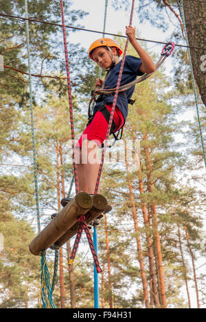 A boy wearing a safety harness and a helmet walking in a rope park ...