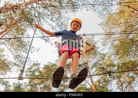 A boy wearing a safety harness and a helmet walking in a rope park ...