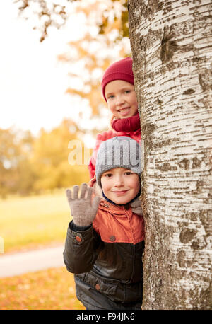 happy children hiding behind tree and waving hand Stock Photo