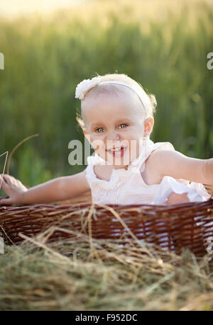 Cute little girl sitting in basket in summer nature Stock Photo