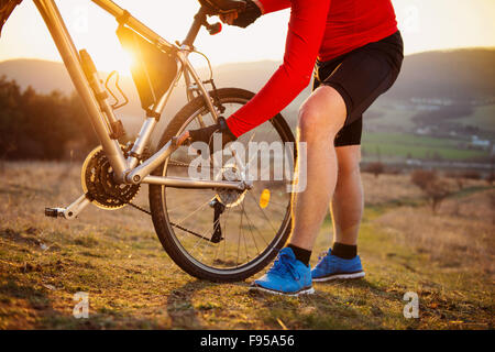 Cyclist man repairing his mountain bike in sunny meadow Stock Photo