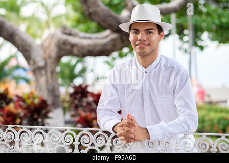 Young hispanic man in formal clothes, wearing white shirt, pants and hat, smiling at camera. Stock Photo