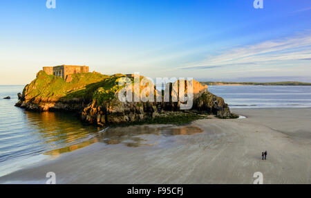 Two people walk on the sands close to St Catherine's Island, Tenby, Pembrokeshire, west Wales, UK Stock Photo