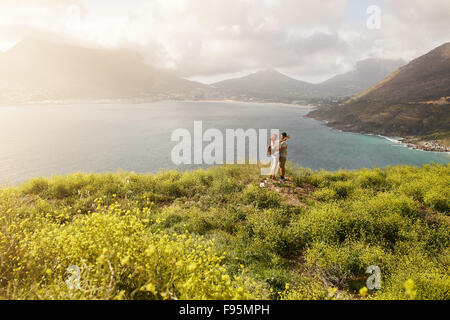 Outdoor shot of romantic young couple standing at the top of a peak. Couple standing close to each other looking into each other Stock Photo