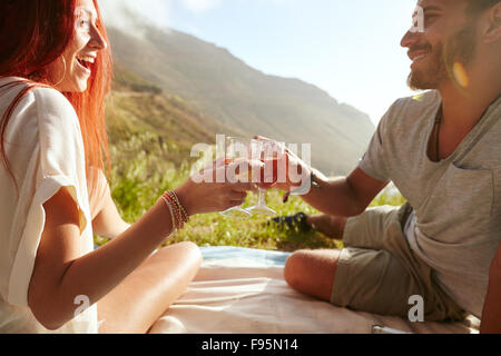 Shot of a cheerful young couple drinking wine and enjoying a picnic. Young man with her girlfriend on vacation sitting on grass