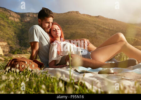 Portrait of loving young couple relaxing on summer picnic. Two young people on a mountain sitting together relaxing. Stock Photo