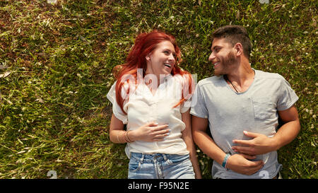Young beautiful couple lying on the lawn and looking at each other smiling. Overhead view of happy young man and woman lying on