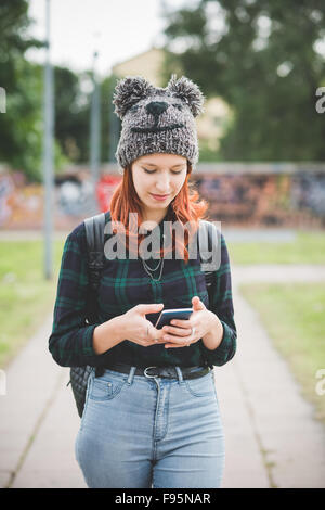 Knee figure of young handsome caucasian redhead straight hair woman walking in the city, holding smartphone, tapping and looking downward the screen - technology, social network, communication concept Stock Photo