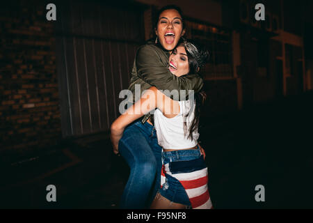 Night shot young woman lifting her best friend laughing. Female friends hanging out and having fun. Stock Photo