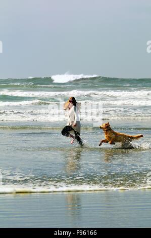 A young woman and her dog (a Golden Retriever) run with a ball in the surf on Chesterman Beach near Tofino, BC. Stock Photo