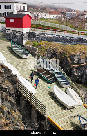 Two fishermen descending a slipway (boat ramp) towards their dory in Pouch cove, Newfoundland, Canada. On the retaining wall Stock Photo