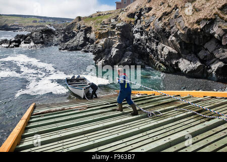 Two fishermen on a slipway (boat ramp) preparing their dory for an outing, Pouch cove, Newfoundland, Canada Stock Photo