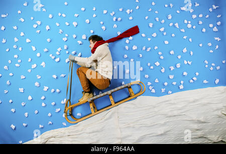 Happy young man on sled having fun against the blue background with snowflakes Stock Photo