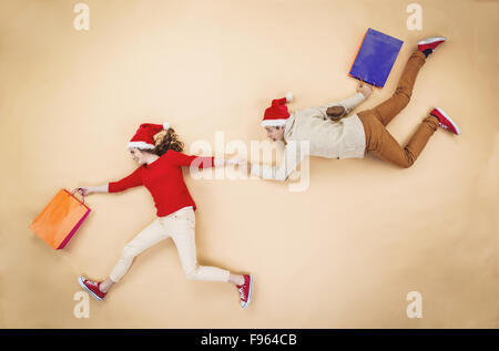 Young couple in Christmas hats having fun running with shopping bags against the beige background Stock Photo