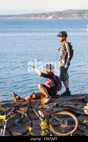 Mountain Bikers taking a break along the Beach Trail watch the sunset, with Sointula in the background.  Port Hardy Stock Photo