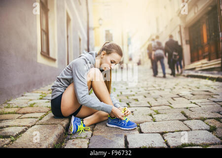 Young female runner is tying her running shoes on tiled pavement in old city center Stock Photo