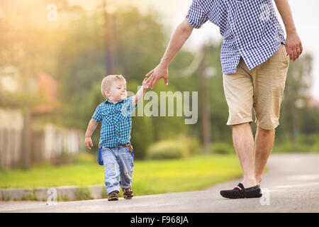 Happy young father holding his little son’s hand and walking on road Stock Photo