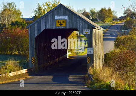 An autumn landscape image showing a one lane wooden covered bridge on a rural road  crossing the Smith Creek near Sussex New Stock Photo