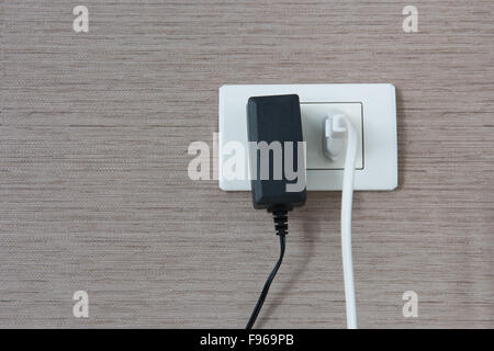 White and black cable plugged in a white electric outlet mounted on wall Stock Photo