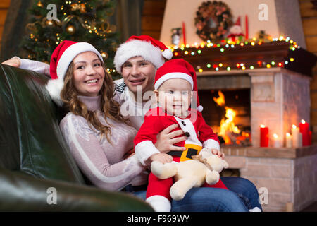 Happy family with child sitting on sofa a fun near Christmas tree and fireplace  in living room Stock Photo