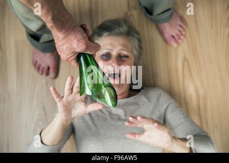 Woman victim of domestic violence and abuse. Mature woman with black eye scared of a man with broken bottle Stock Photo
