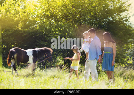 Portrait of young happy family at countryside outdoors, feeding pony