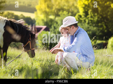 Portrait of young happy father with his dauhter at countryside outdoors, feeding pony Stock Photo