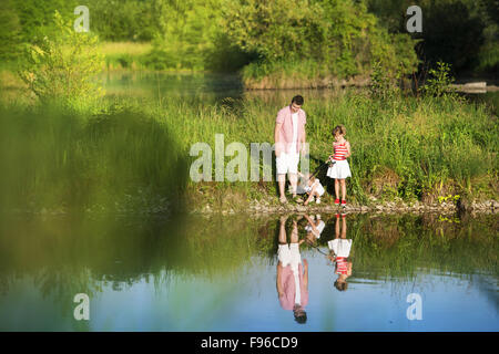 Happy young father fishing on the lake with his little daughters, reflecting in the water Stock Photo
