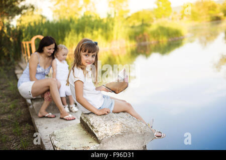 Two little sisters and their mom playing with paper boats on lake Stock Photo