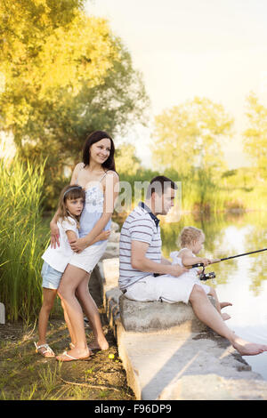 Young happy family with kids fishing in pond in summer Stock Photo