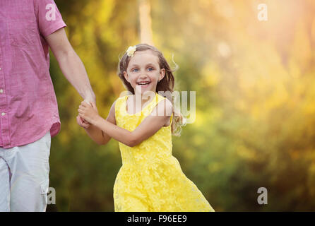 Happy little girl holding dad's hand and walking in the park Stock Photo