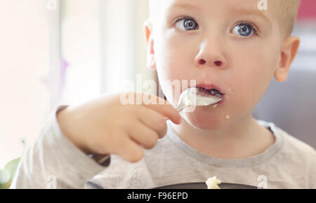 Cute little blonde boy eating pasta from black bowl Stock Photo