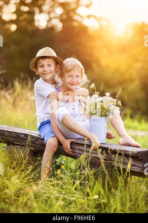 Cute boy and girl in love. They sitting on bench at sunset. Stock Photo