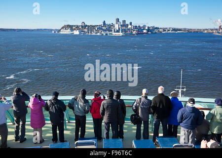 Passengers on the top deck of a cruise ship watching as their vessel makes its way towards Quebec City in the distance Stock Photo