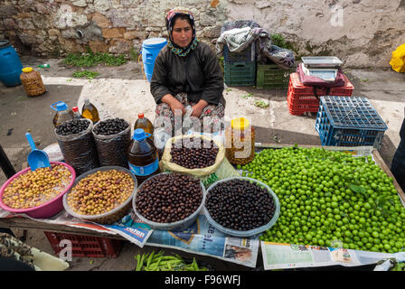 A woman with traditional clothes sells olives and fruits in the open market of the city on April 24, 2014 in Ayvalik, Turkey. Stock Photo