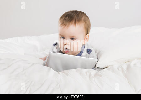 Baby with digital tablet is playing in the bed Stock Photo