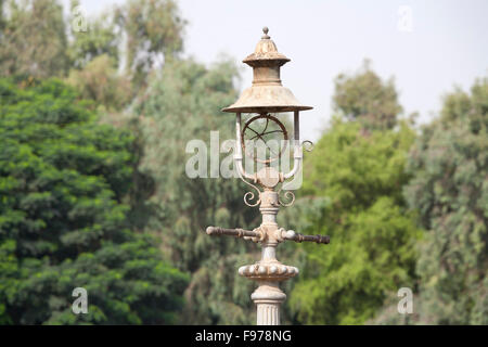 A Victorian style gas mantle street light converted into electric lighting but broken and neglected against a tree background Stock Photo