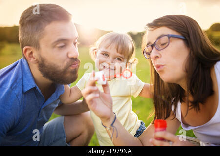 Happy little girl with her parents blowing bubbles in summer nature Stock Photo
