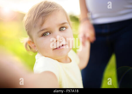 Little girl with mum in background taking selfie by mobile phone Stock Photo