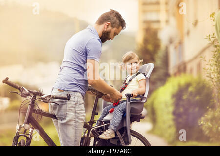 Young father with his little daughter on bicycle in green sunny park Stock Photo