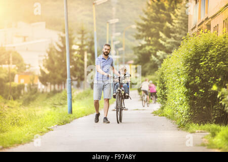 Young father with his little daughter on bicycle in green sunny park Stock Photo