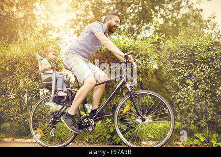 Young father with his little daughter on bicycle in green sunny park Stock Photo