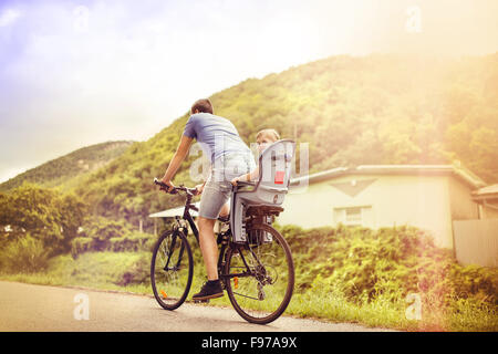 Young father with his little daughter on bicycle in green sunny park Stock Photo
