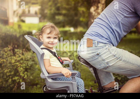 Young father with his little daughter on bicycle in green sunny park Stock Photo