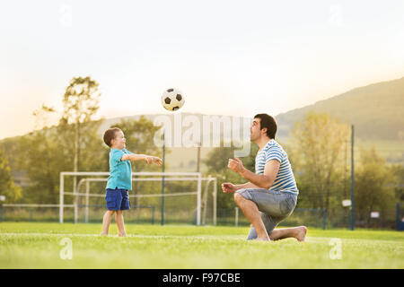 Young father with his little son playing football on football pitch Stock Photo