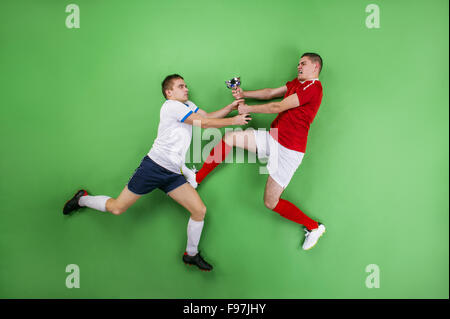 Two enthusiastic football players fighting for a trophy. Studio shot on a green backgroud. Stock Photo