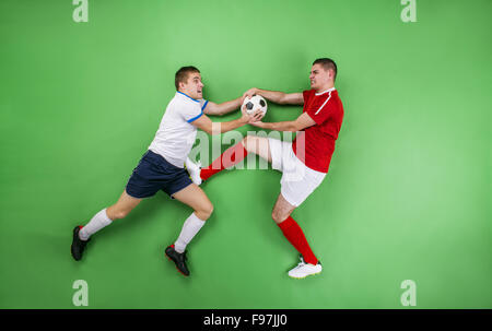 Two enthusiastic football players fighting for a ball. Studio shot on a green backgroud. Stock Photo