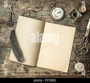 Open book and vintage office supplies on wooden table. Feather pen, inkwell, keys on textured background. Retro style toned pict Stock Photo