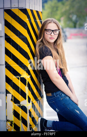 Teenage hipster girl standing by the black and yellow striped warning wall Stock Photo